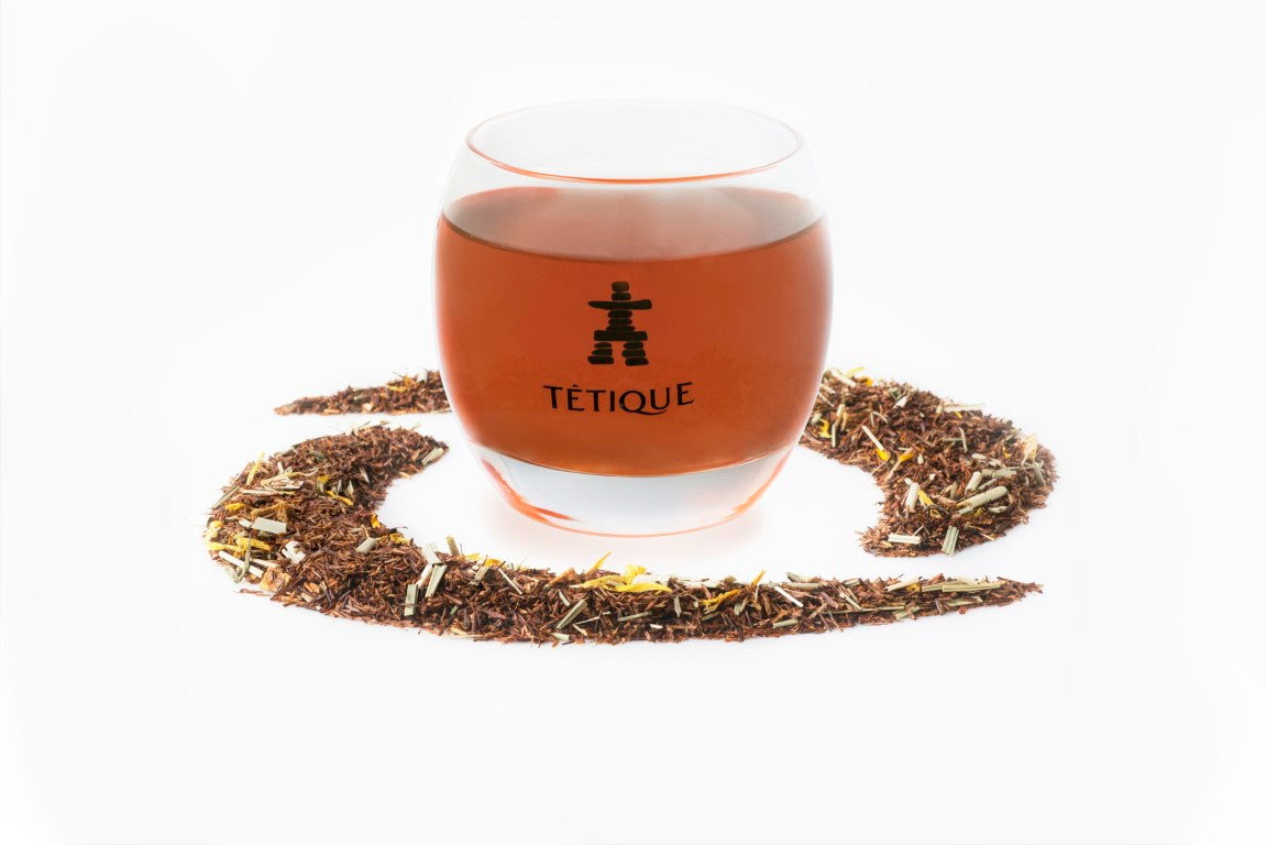Infusión Rooibos Mango Fresa biológica a granel, 240 gr. en una taza de vidrio junto a hojas de rooibos.