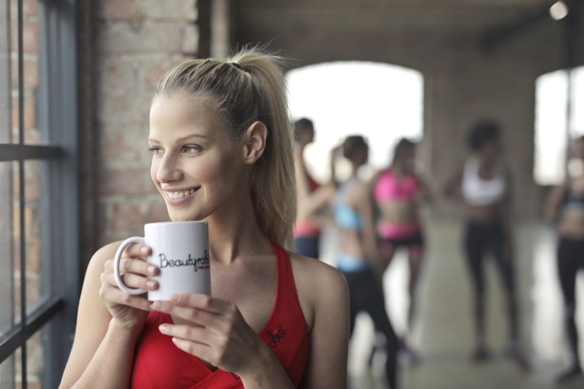 Mujer joven bebiendo taza de té ecológico en el gimnasio